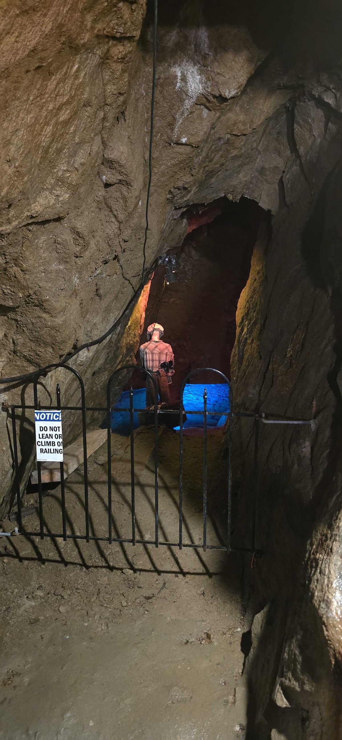 Mannequin of a miner in plaid shirt and hard hat standing near a blue-lit shaft