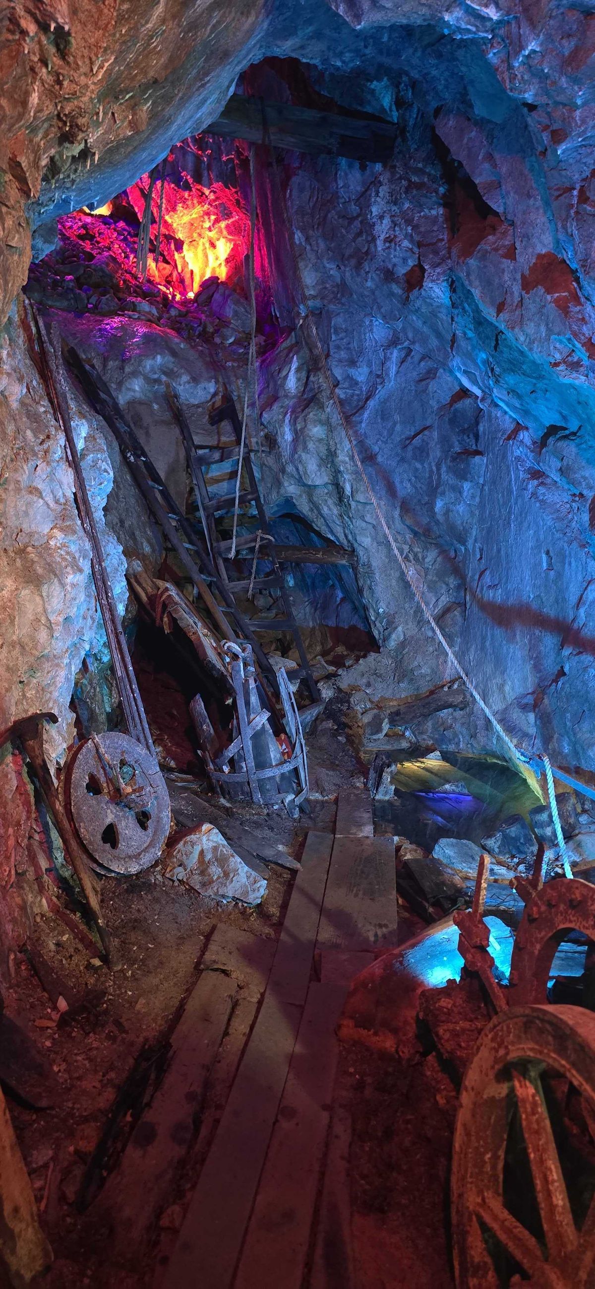 Original mining equipment inside a stope — ore cart wheels, ladders, and hoisting gear lit with colored lights